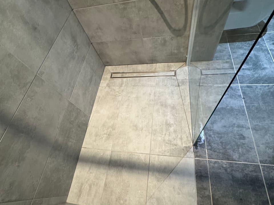 Douche à l'italienne avec receveur carrelé, caniveau inox et paroi vitrée posée par KAT Plomberie dans le Chablais